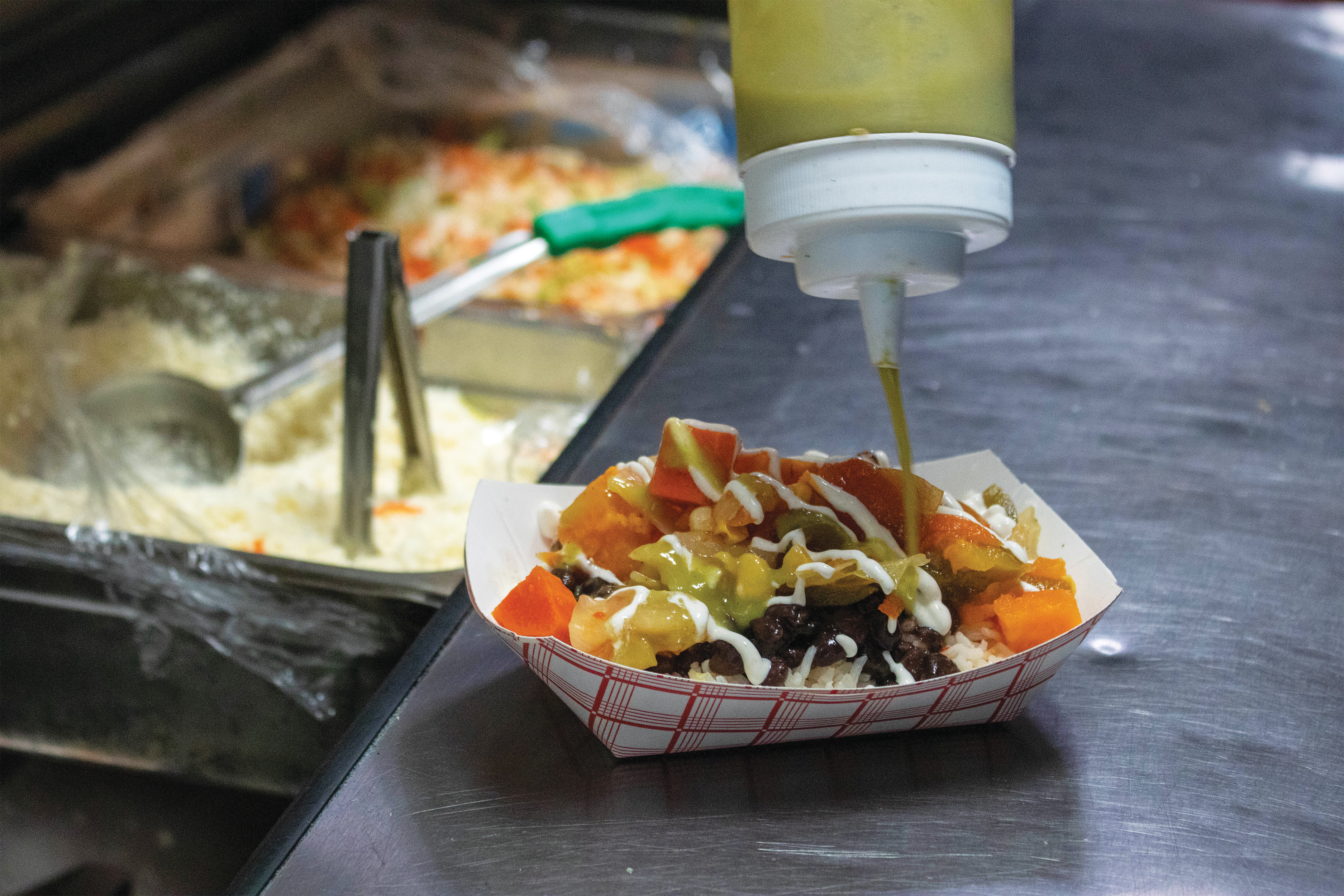 A squeeze bottle drizzling sauce on top of a meal in the food truck